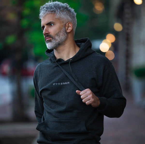 man modeling grey hoodie with embroidered white text, "MT913 Sinner."